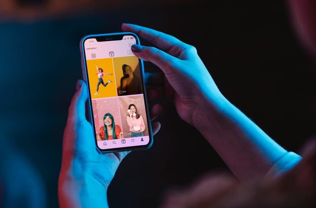 Person holding a phone, browsing through a grid of social media posts